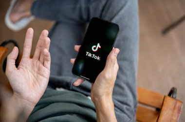 Chiang Mai, Tayland - 8 Mayıs 2025 TikTok uygulaması ile akıllı telefonu elinde tutan bir adama yaklaş. Bankta oturup, canlı ya da video izliyorum..