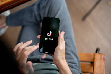 Chiang Mai, Tayland - 8 Mayıs 2025: TikTok uygulamasını kullanarak akıllı telefonu tutan bir adama yaklaş. Bankta oturup, canlı ya da video izliyorum..