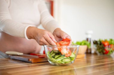 Hamile Asyalı kadının domates dilimlerini cam kaseye koyup mutfakta sebze salatası yapmasını yakından çek. Doğum öncesi bakım, Hamilelik Diyet yemeği.