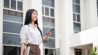 Üniversite ya da ofis binasından çıkarken elinde telefon ve laptop tutan Asyalı bir kadın. Okuldan ayrılan öğrenci, işten çık..