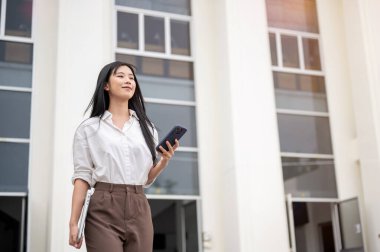 Beyaz tişörtlü Asyalı kadın üniversite veya ofis binasından çıkarken önüne bakıyor. Okuldan ayrılan öğrenci, işten çık..