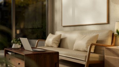 Deri bir kanepenin arkasındaki duvarda boş bir çerçeve ve oturma odasındaki cam kapılı ahşap masada bir dizüstü bilgisayar. 3B görüntüleme, 3B Görüntü.