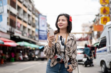 Asya 'lı turist bir markette yol kenarında dikilirken bir eli cebinde akıllı telefondan kafasını çeviriyor. Yürüyen cadde, Eski kasaba gezisi.