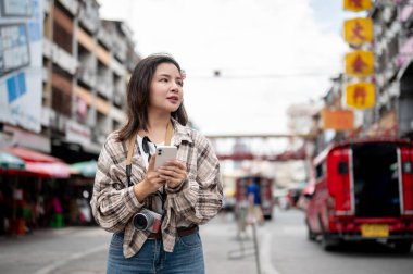 Asyalı turist kadın, iki eliyle bir markette yolun kenarında dikilirken telefonla konuşurken gergin görünüyor. Yürüyen cadde, Eski kasaba gezisi.