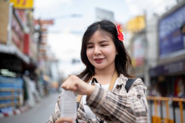 Saçında kırmızı amber çiçeği olan Asyalı bir turist içmek için serin bir su şişesini yerel pazarda duruyor gibi açıyor. Yürüyen cadde, Eski kasaba gezisi.