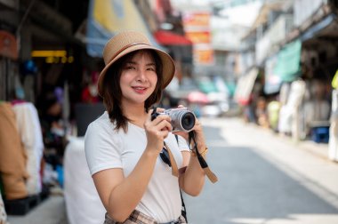 Asyalı turist kadın elinde kamerayla eski markette fotoğraf çekerken gülümsüyor. Turistik bir yer, Yürüyen bir sokak, Eski bir kasaba gezisi.
