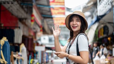 Yerel markette kaldırımda elini sallarken gülümseyen Asyalı turist kadın. Turistik bir yer, Yürüyen bir sokak, Eski bir kasaba gezisi.
