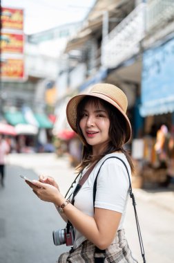 Asyalı turist kadın telefonunu kaldırımda tutarken gülümseyen bir şapka takıyor. Turistik bir yer, Yürüyen bir sokak, Eski bir kasaba gezisi.