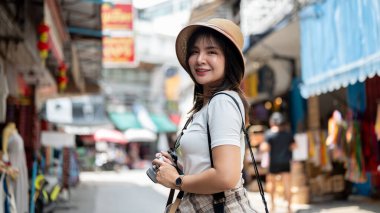 Kamerasını tutarken gülümseyen Asyalı kadın iki eliyle eski markette dikiliyor. Turistik bir yer, Yürüyen bir sokak, Eski bir kasaba gezisi.