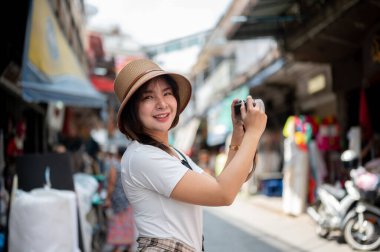 Asyalı turist kadın elinde kamerayla gülümserken markette fotoğraf çekiyor. Turistik bir yer, Yürüyen bir sokak, Eski bir kasaba gezisi.