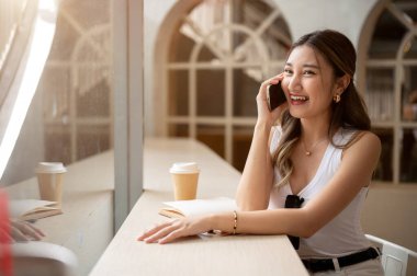 Not defteri ve kahve fincanıyla ahşap masanın üzerinde gülüp etrafa bakan Asyalı bir kadın. Kafede takılıyorum, Kentsel yaşam tarzı.