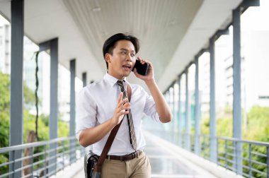 İş adamı ya da ofis çalışanı yaya köprüsünde yürürken ve etrafa bakarken telefonla konuşuyor. Git ya da işi bırak, modern şirket işleri..