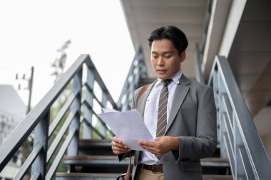 İşadamı ya da ofis çalışanı elindeki belgelere bakıyor üstgeçitte ya da üst geçitte duruyor. Git ya da işi bırak, yüksek metal köprü..