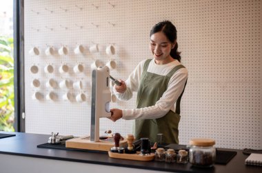 Asyalı kadın barmen yeşil önlüklü, el presi makinesi kullanan ya da tezgahta kahve yapan. Sıcak içecek, kafe ya da kahve dükkanı, küçük işletme..