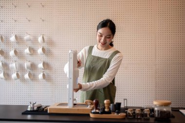 Yeşil önlüklü Asyalı bayan barista tezgâhta kahve yapmak ya da kahve yapmak için el presi makinesi kullanıyor. Sıcak içecek, kafe ya da kahve dükkanı, küçük işletme..