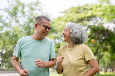 Koşarken ya da parkta koşarken gülümseyen ya da gülen gözlüklü yaşlı adam ve yaşlı kadın. Yaşlı çift, Yeşil Doğa, Serinleyen Açık Hava.