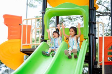 Asyalı kız ve erkek kardeşler parkın oyun parkında renkli tırmanma slaytlarında oynuyorlar. Yaratıcı Oyuncaklar, sevimli çocuklar, Aile Gezisi.