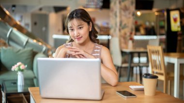 Güzel Asyalı kadın ellerini çenesinin altına sıkıştırıp kafeteryada ya da kantinde dizüstü bilgisayara bakıyor. Çalışmak ya da çalışmak, dışarıda dinlenmek, günlük hayat..