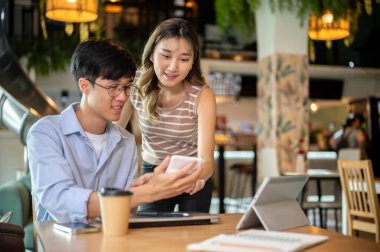 Asyalı bir kadın, bir kafede ya da kantinde, bir adamın hesap makinesine bakıp, tahta masanın üzerine eğiliyor. Çalışma ya da öğrenim, Görev ya da Grup Projesi.