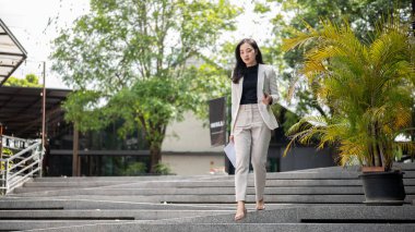 Asyalı kadın ofis çalışanı ya da elinde bilgisayarla beton merdivenlerden aşağı inen bir iş kadını. Şirket işi, modern şirket, dışarı çıkmak..