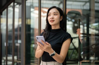 Asyalı üniversite öğrencisi ya da kadın ofis çalışanı elinde telefonla kafe ya da kahve dükkanının önünde bekliyor. Bir arkadaşla buluşmak, günlük hayat, dışarı çık..