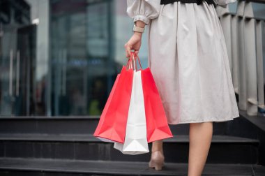 Bir kadının ya da ofis çalışanının elinde kırmızı kağıt poşetlerle alışveriş merkezine doğru merdivenlerden çıkarken görüntüsü. Maaş günü, marka reklamı, şehir hayatı..