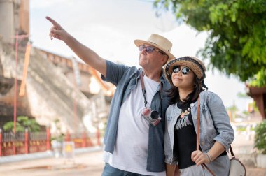 Kot giymiş yaşlı beyaz bir çift Budist tapınağındaki tapınağa bakan bir kadını işaret ediyor. Chiang Mai, Tayland, Turist Çekimleri.