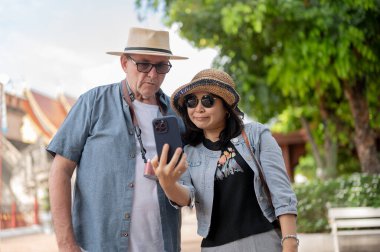 Kot pantolonlu yaşlı beyaz bir adam Asyalı bir kadının elini tutarak fotoğraf çekiyor. Chiang Mai, Tayland, Turist Çekimleri.