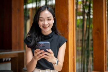 Asyalı kadın kulaklık takıyor, video izliyor ya da kafenin ahşap koridorunda bambu bahçesinin yanında telefonla konuşuyor. Boş zaman, dışarıda dinlenme zamanı.