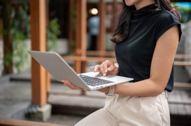 Açık kafedeki bahçe avlusundaki ahşap bankta otururken elinde dizüstü bilgisayar tutan ve kullanan kadın öğrencilere yakın çekim. Çalış ya da çalış, dışarıda takıl..