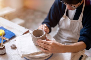 Çömlek sanatçısı, sınıftaki ya da stüdyodaki çalışma masasının tekerindeki kilden kupaya doku eklemek için fırça kullanıyor. Seramik Yapım, El yapımı Ürün, Sanat Atölyesi.