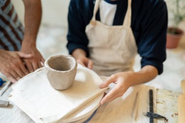 Sınıfta ya da stüdyoda çalışma masasında öğrencinin kilden kupasına bakan çömlek öğretmeni. Seramik Yapım, El yapımı Ürün, Sanat Atölyesi.