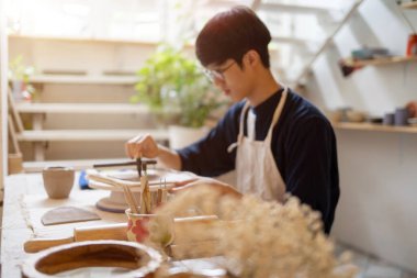Gözlüklü genç çömlekçi ressam çömlekçilik ya da stüdyo odasında çalışma masasında kil kesiyor. Seramik Yapım, El yapımı Ürün, Sanat Atölyesi.