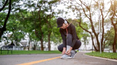 Spor giyim ve kulaklıklı genç Asyalı kadın spor yapmadan önce spor ayakkabı bağcığını bağlıyor ya da parkta egzersiz yapıyor. Sağlıklı yaşam, kamusal alan, yeşil manzara.