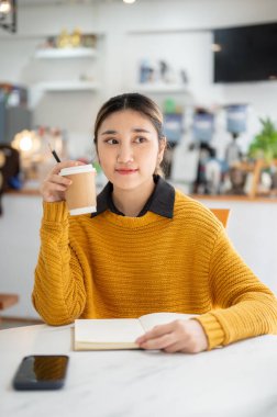 Kafe 'nin masasında otururken elinde kahve tutan Asyalı kadın telefonu bir kenara bırakıp telefona bakıyor. Çalışmak ya da Çalışmak, Dışarıda Takılmak, Şehir Hayatı.