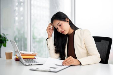 Sıkıcı Asyalı iş kadını ya da ofis çalışanı. Çalışma masasında dizüstü bilgisayarın önünde saçlarını tarıyor. Masa başı işleri, şirket çalışanı, modern şirket..