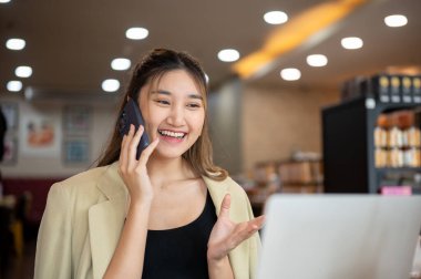 Kafedeki ahşap masada otururken dizüstü bilgisayara bakan gülümseyen Asyalı kadın. Çalışmak ya da çalışmak, şehir hayatı, dışarıda dinlenmek..