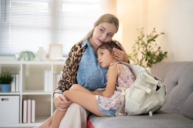 Beyaz tenli anneler bir oturma odasında kanepede otururken küçük kıza sarılıp okşuyor. Ebeveynlik, karışık ırk ailesi, ilkokul öğrencisi..