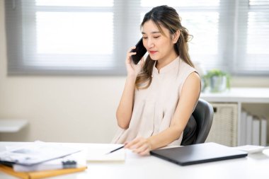 Güzel bir kadın ofis çalışanı elinde akıllı telefonla ofisteki bir arkadaşıyla ya da iş arkadaşıyla konuşuyor. İş Gelişigüzel, Modern Şirket, Şirket İşi.