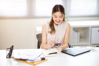 Gülümseyen kadın ofis çalışanı elinde akıllı telefonla sosyal medyayı kullanıyor ya da ofiste sohbet ediyor. İş Gelişigüzel, Modern Şirket, Boş zaman.