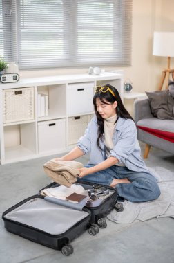 Asyalı bir kadın bavuluna katlanmış kumaş koyuyor. Yatak odasında ya da oturma odasında toplanırken. Seyahat Gezisi, Turist Çantası, Çanta Düzenleme.