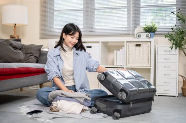 Asyalı bir kadın yatak odasında ya da oturma odasında otururken bavulları düzenlemek ya da paketlemek için bavul açıyor. Seyahat Gezisi, Turist Çantası, Çanta Düzenleme.