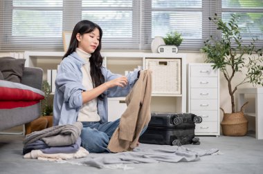 Kumaş katlayan Asyalı kadın ya da yatak odasında ya da oturma odasında yere inmek için bavul hazırlayan. Seyahat Gezisi, Turist Çantası, Çanta Düzenleme.