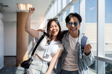 Heyecanlı Asyalı turist çifti havaalanında ayakta dikilirken gezgin kadınla sevişip yumruklarını kaldırıyorlar. Yurtdışına seyahat, hava yolcusu, tatil tatili.