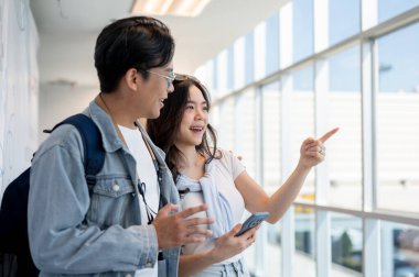Asyalı turist çift geziye çıkıyor. Elinde telefonla konuşan ve havaalanında bir adamı işaret eden bir kadın. Yurtdışına seyahat, hava yolcusu, tatil tatili.