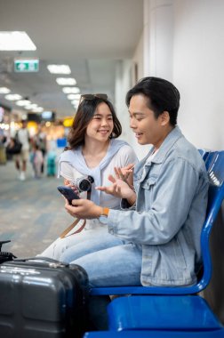 Asyalı turist çift, havaalanında beklerken kadınla konuşan ve telefonlarına bakan bir adamla seyahate çıkıyor. Yurtdışına seyahat, hava yolcusu, tatil tatili.