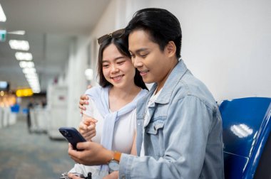 Asyalı turist çift, gezgin bir adama sarılıp havaalanında beklerken telefona bakıyorlar. Yurtdışına seyahat, hava yolcusu, tatil tatili.