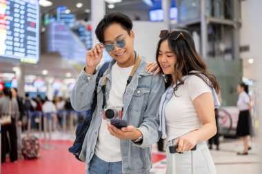 Adamın telefonuna bakan Asyalı bir çift turist havaalanından ayrılmayı bekliyor. Yurtdışına seyahat, hava yolcusu, tatil tatili.