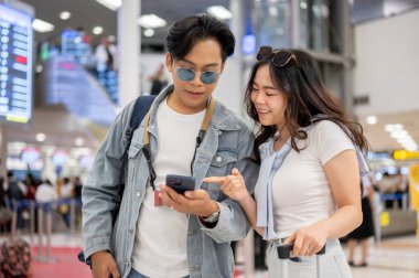 Asyalı çift turist erkeğin telefonunu işaret ederek havaalanından ayrılmayı bekliyor. Yurtdışına seyahat, hava yolcusu, tatil tatili.