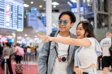 Asyalı çift turist, havalimanında kalkmayı beklerken bir adamı işaret ediyor. Yurtdışına seyahat, hava yolcusu, tatil tatili.